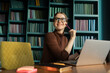 © muse studio - The workplace video communication manager uses a laptop computer. A student with glasses in the office in the library.