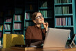 © muse studio - A student with glasses in the office in the library. Workplace video communication manager uses laptop computer.