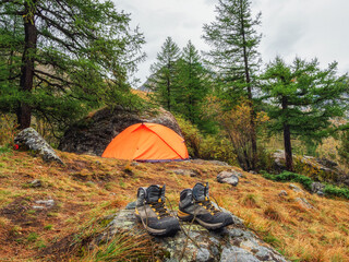 Wet hiking boots to dry. Atmospheric mountain landscape with tent under tree on hill in autumn colors in dense fog.