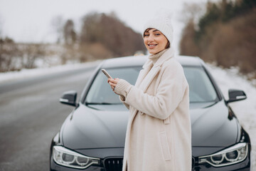 Woman talking on the phone by her car on the road in winter forest