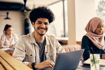 Wall Mural - Happy Muslim student uses laptop in cafeteria at campus and looking at camera.