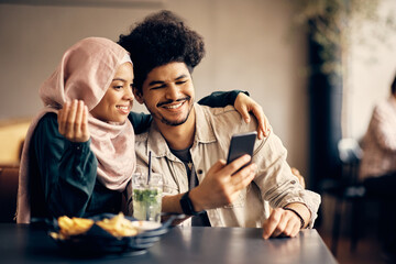 Wall Mural - Happy Muslim man and his girlfriend use smart phone in cafe.