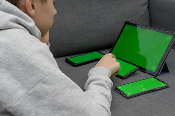 Teenage boy using multiple electronic internet devices in same time. Kid watching something on digital tablet, playing on cell phones at home. Multi screening, engaging in multiple gadgets at once