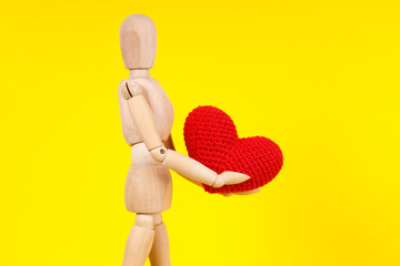 Poster - wooden man with a red heart in his hands on a yellow background