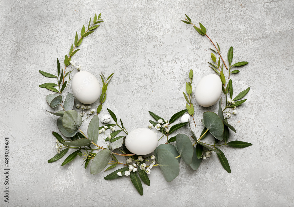 Stylish wreath with Easter eggs, eucalyptus leaves and flowers on light background