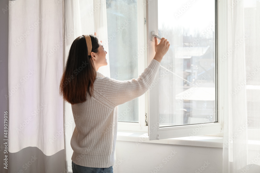 Pretty young Asian woman opening window at home