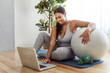 © Louis-Paul Photo - African american woman working out in home livingroom gym with laptop