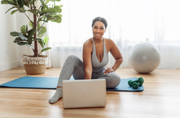 Wall Mural - African american woman working out in home livingroom gym with laptop