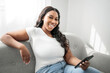 © Louis-Paul Photo - Attractive young African woman sitting on the couch at home with cellphone