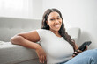 © Louis-Paul Photo - Attractive young African woman sitting on the couch at home with cellphone