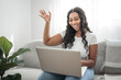 © Louis-Paul Photo - Attractive young African woman working on laptop while sitting on the couch at home say hi