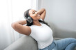 © Louis-Paul Photo - Attractive young African woman sitting on the couch at home listening music with headphone