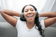 © Louis-Paul Photo - Attractive young African woman sitting on the couch at home listening music with headphone