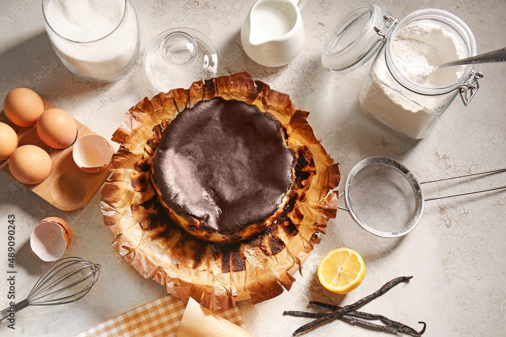 Tasty Basque burnt cheesecake with ingredients on light background
