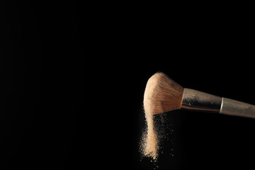 Makeup brush shaking off powder on black background