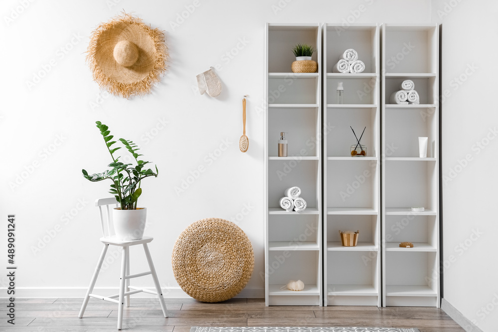 Interior of light bathroom with shelving unit and rattan pouf