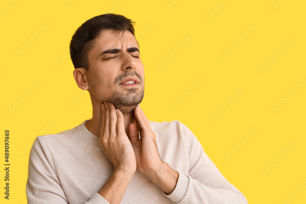 Ill young man with sore throat on yellow background