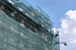 © bilanol - Building facade under renovation works with construction scaffolding frame covered with protective net for workers safety