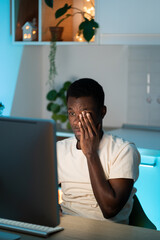 Tired or bored african american male worker or student sit at desk need rest suffer from fatigue overworked at home. Exhausted man working at computer late at night try to meet deadline on project