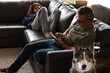 Father and teenage daughter sit on couch using mobile phones