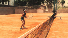 A Side View Of A Slim Young Brazilian Female Practicing Tennis On A Court: Standing On An Orange Clay Ground Next To The Net, With The Racquet In Hands Ready To Hit The Ball; Leme, Rio De Janeiro