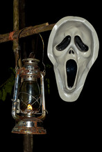 Scary Halloween Scream Ghost-face Dead Mask On A Black Background With An Old Kerosene Lantern Hanging On The Dead Dry Wood For Light In Forest At Night