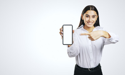 Mobile application concept with happy girl in white shirt showing modern cellphone with white blank screen on abstract light gray background with place for your logo or text, mockup