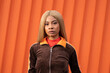 © Sergio Mena - Joven mujer afroamericana con cabello largo rubio y ropa deportiva sobre un fondo de color naranja