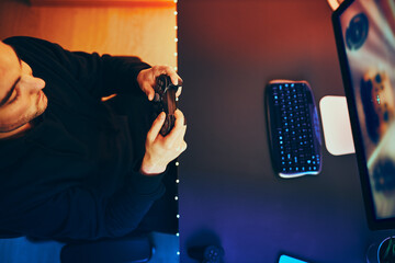 Wall Mural - Man playing video game at home. Gamer holding gamepads sitting at front of screen. Streamer playing online in dark room lit by neon lights. Competition and having fun