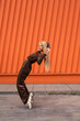 © Sergio Mena - Una alegre mujer afroamericana con ropa deportiva bailando en la calle sobre un fondo naranja