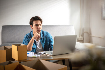 Serious upset young man entrepreneur at home works on a laptop computer and online checks no orders to pack the parcel boxes, sell to customers, Online Selling shopping, and business ideas online