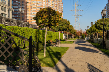 Wall Mural - Pedestrian recreation area with benches, lawns and trees. Residential complex Turgenev. High voltage power lines. Houses and road behind forged fence. Krasnodar, Russia - October 27, 2021