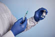 Doctor prepares American covid vaccine shot. Medic guy with coronavirus inoculation phial from USA and injection syringe in hands. Medic palms in blue gloves. Photo with blue gradient background.