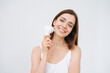 Beauty portrait of happy smiling woman with dark long hair with facial massager in hand on clean fresh skin face on the white background isolated
