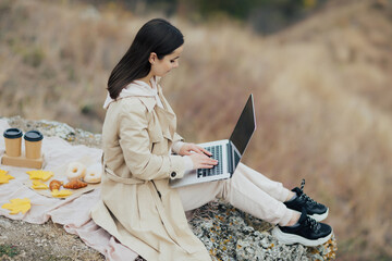 Wall Mural - Woman with laptop computer is taking autumn picnic. Coffee and donuts on the blanket.