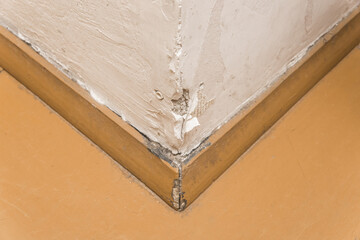 A dowel nail is a fixing building in a white cement wall. Repair of the corner joint angle next to the wooden plinth floor baseboard flooring of the concrete construction industry structure