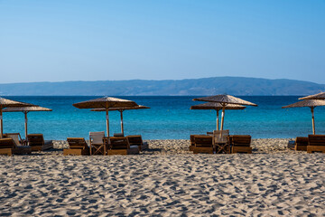 Wall Mural - Summer holiday at seaside. Straw umbrella lounger in row on sandy empty beach sunny day.