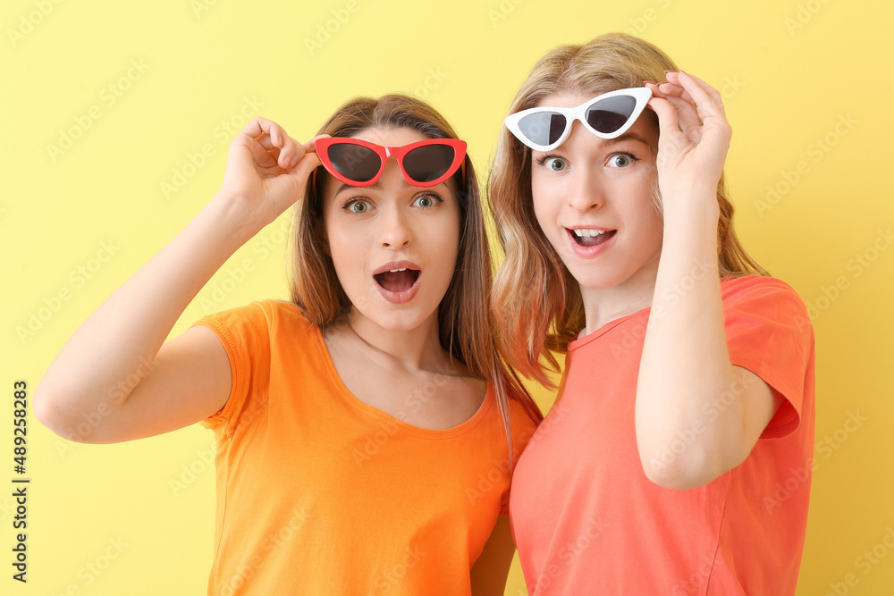 Portrait of surprised young sisters on color background