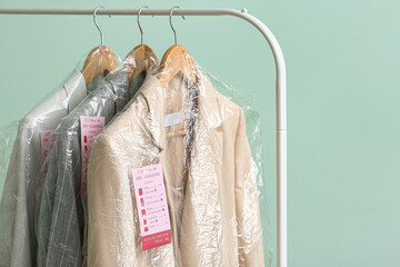 Poster - Rack with clean jackets in plastic bags on green background, closeup