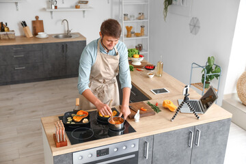 Wall Mural - Young man cooking tasty vegetables while recording video tutorial in kitchen