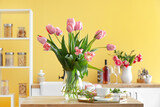 Fototapeta Tulipany - Vase with tulips, gift box, cup of coffee and macarons on table in kitchen