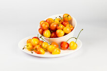 Ripe Sweet Rainier Cherries In A White Bowl And On Plate On White Background.