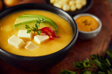 Wall Mural - Ecuadorian locro de papa a traditional potato and cheese soup served with avocado and hominy. It’s on a wooden background