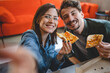 © Miljan Živković - two people young couple man and woman or friends sitting at home at the table taking selfie photos with mobile phone smartphone while eating pizza spending time together having fun bonding in love