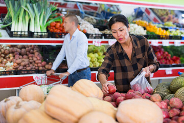 European man and Asian woman choosing vegetables and fruits in supemarket.