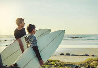 the waves are waiting. shot of two young brothers holding their surfboards while looking towards the