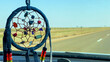 Dream catcher hanging from rear view mirror of car with road in the background. Hippie road trip. Adventure journey and wanderlust concept