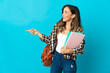 © luismolinero - Young student woman isolated on blue background pointing finger to the side and presenting a product