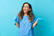 © luismolinero - Woman dentist holding tools over isolated on blue background with shocked facial expression