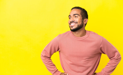 Wall Mural - Young latin man isolated on yellow background posing with arms at hip and smiling